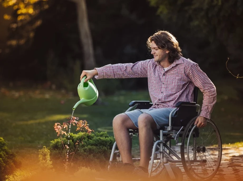 Happy disabled man in wheelchair outside watering plants